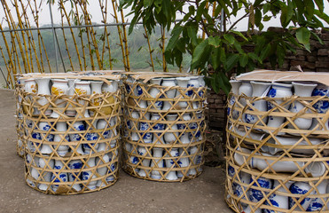 three crates of ceramic vases packed up and ready to ship on side of river with bamboo 