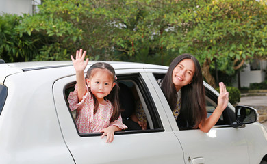 Mother and little child girl sitting on a car looking camera and waving goodbye. Holiday concept.