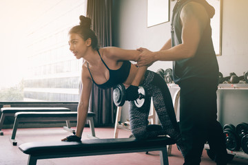 Personal training men help women's arms to pull up dumbbell for exercise at indoor gym.
