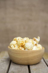 Fresh salted popcorn in round wooden bowl on wooden table over blurred hessian fabric background, movie night snack