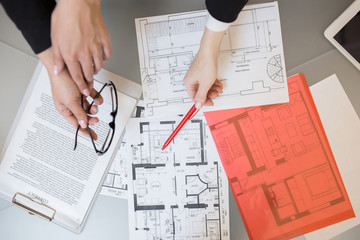 Above view close up of unrecognizable people pointing at house plans on table in real estate agency