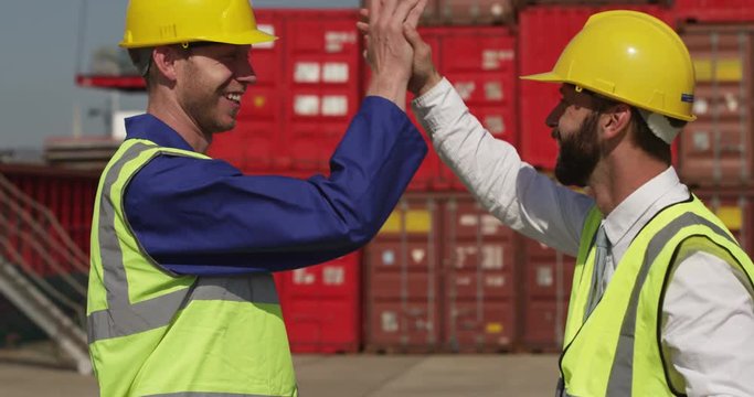 A docker and a supervisor celebrate with a high five at an industrial harbor. Shot on RED Epic.