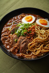 Japanese ramen with pork belly, mushrooms and marinated eggs on green linen tablecloth