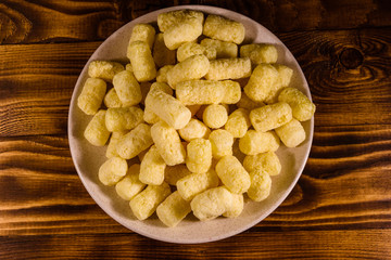 Ceramic plate with corn sticks on wooden table. Top view