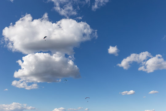 Some paragliders flying against a beautiful deep, blue sky, with big white clouds
