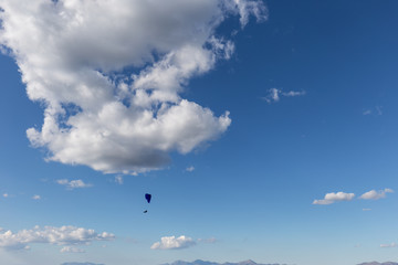 A paraglider flying against a beautiful deep, blue sky, with big white clouds
