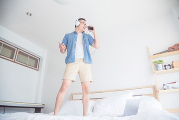 Young asian man listening music from smart phone via headphones in bedroom