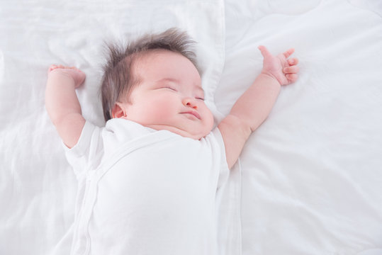 Little asian infant stretching on white bed in the morning