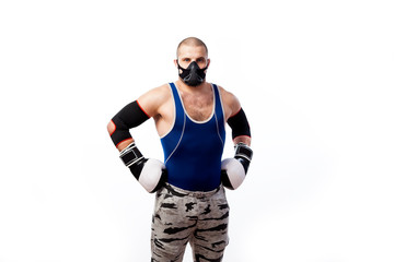 A young sporty man in blue tights, a black training mask, black-and-white boxing gloves and black elbow pads is on a white isolated background, his hands are at the waist