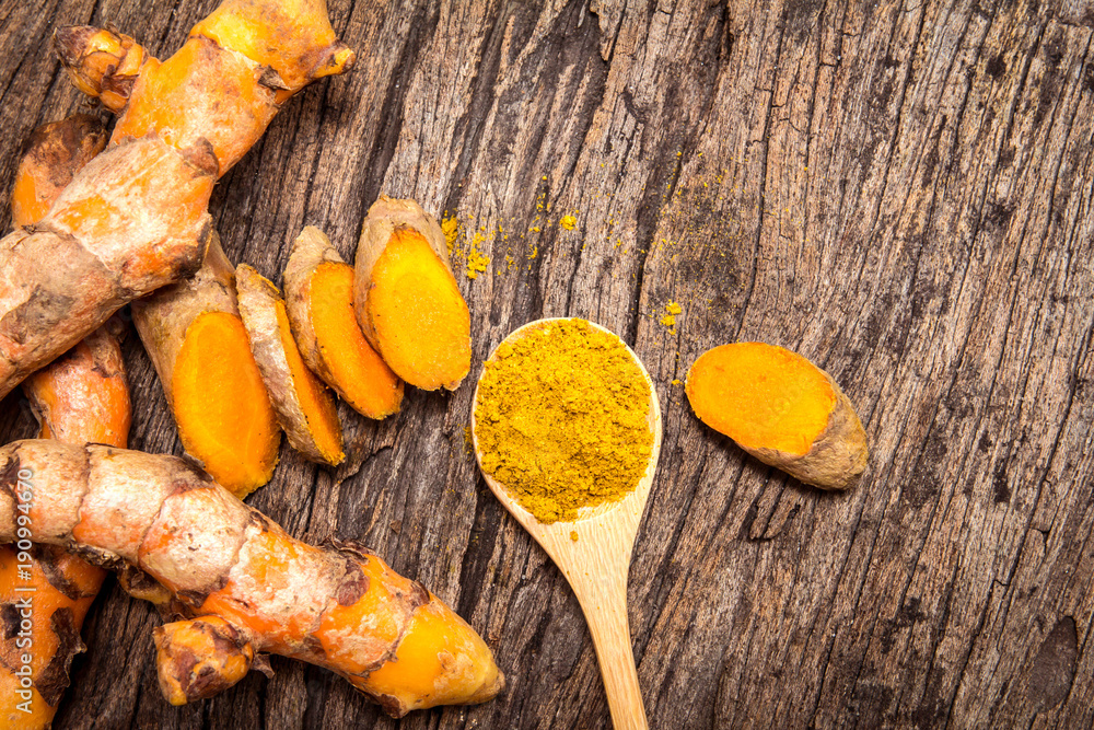 Poster turmeric powder in spoon and roots on wooden plate