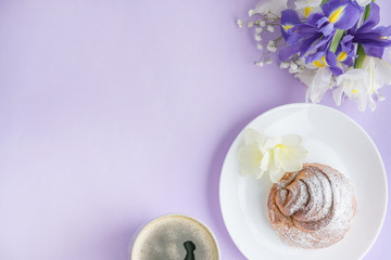 Morning Cup of coffee cup and a delicious bun beautiful flowers. flat lay image on pink table from above. Female working desk. Cozy breakfast style. Top view office desk. Workspace purple composition