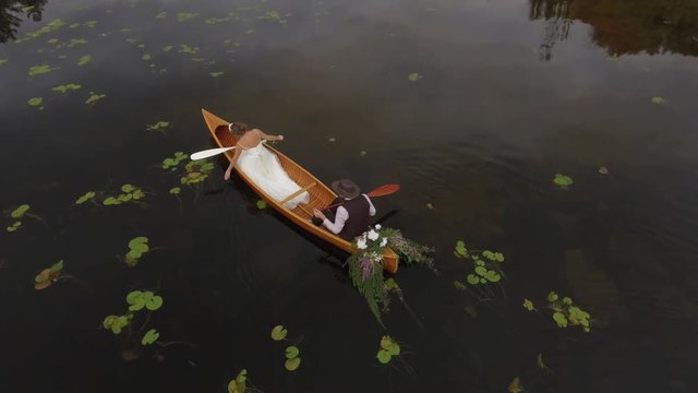 newly weds canoe close up as bride drags hand in water aerial 4k