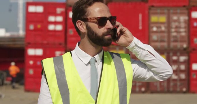 A confident dock worker talking on a mobile phone at an industrial shipyard. Shot on RED Epic.