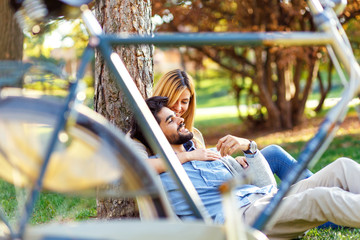 Young couple in love sitting in a autumn park leaning against a tree embracing one another.