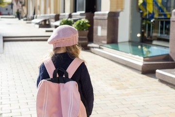 Stylish little girl with backpack, in a coat and french beret run to school. Back view