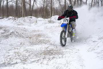 Sportsman racer man fulfills a fast ride on a motorcycle on the road extreme. The race track is very uneven. Cloudy winter day with a snowstorm.