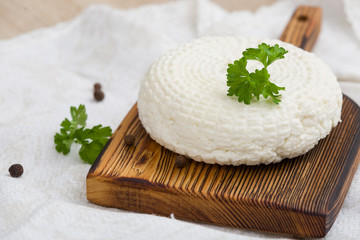 Closeup of round white homemade cheese - traditional milk creamy dairy product served with herbs on...