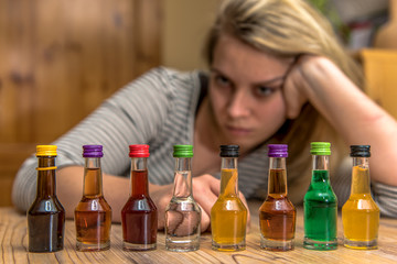 Fototapeta premium A woman (25-30) is sitting in front of many small bottles of alcohol. Concept: alcohol abuse or drinking