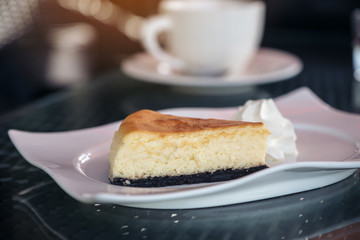 A piece of cheese cake and whipped cream in white plate with coffee cup on table in cafe