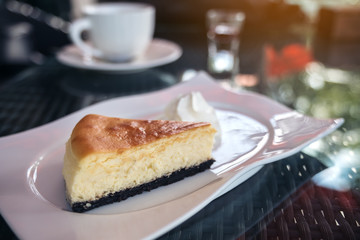 A piece of cheese cake and whipped cream in white plate with coffee cup on table in cafe