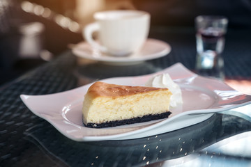 A piece of cheese cake and whipped cream in white plate with coffee cup on table in cafe