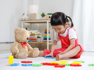 Preschooler girl learns at school. Cute child playing with teddy bear. Little girl having fun indoors at home, kindergarten or