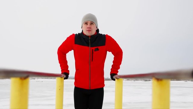 A sports trained man performs push-ups on parallel bars in the winter in the open air.