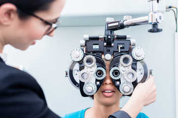Optometrist and woman at eye examination with phoropter - obrazy, fototapety, plakaty