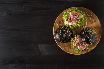 Black burger with salmon fish, lettuce, mustard. Dark background. Fast food.