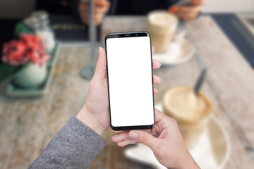 Smart phone mockup in woman hands. Coffee shop in background, table and plant. Big screen with round edges.