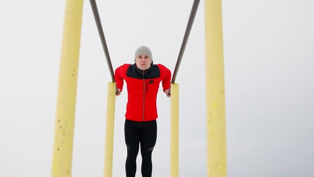 A sports trained man performs push-ups on parallel bars in the winter in the open air. Bottom view of the overall plan. 120 frames per second. Close-up.