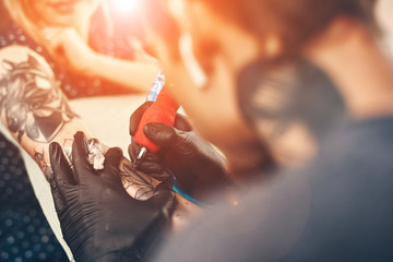 A young guy, beats a tattoo on the hand of the girl in a tattoo parlor, rotary tattoo machine,...