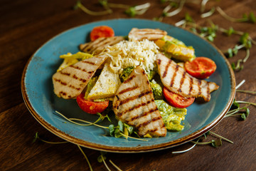 A horizontal image of a salad with grilled turkey, tomatoes, cheese, crusty white bread and mango mayonnaise, served on a blue plate, decorated with greenery. Selective focus.