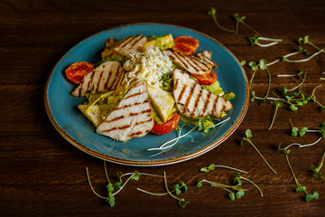 A horizontal image of a salad with grilled turkey, tomatoes, cheese, crusty white bread and mango mayonnaise, served on a blue plate, decorated with greenery. Selective focus.