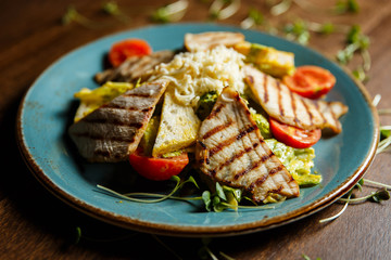A horizontal image of a salad with grilled turkey, tomatoes, cheese, crusty white bread and mango mayonnaise, served on a blue plate, decorated with greenery. Selective focus.