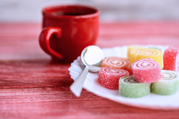 colorful marmalade and a cup of coffee on a red wooden background