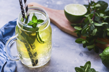 Cold beverage mojito in a glass jar with lime and mint on a table.