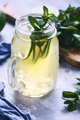 Cold beverage mojito in a glass jar with lime and mint on a table.