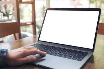 Mockup image of a hand using and touching laptop with blank white desktop screen on wooden table in cafe