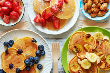Top view of assorted pancakes with strawberry, blueberry, banana, honey and nuts. Breakfast for 3...