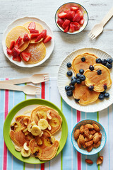 Top view of assorted pancakes with strawberry, blueberry, banana, honey and nuts. Breakfast for 3 person.
