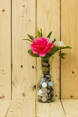 Red roses in a clear bottle filled with silver coins. And the plank is the background. , A tree concept that grows with money.