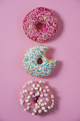 Three various donuts line on a pink background. One of them has a bite on it. Sweetness happiness conception. 