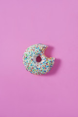 A bagel with a bite on pink isolated background. Top view. Sweetness, happiness concept.