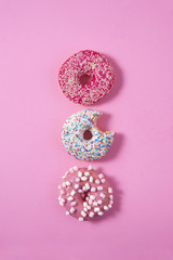 Three various donuts line on a pink background. One of them has a bite on it. Sweetness happiness conception. 
