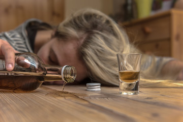 A woman (25-30) fell asleep drunk at the table. Alcohol runs out of a brandy bottle. Concept: alcohol abuse or drinking