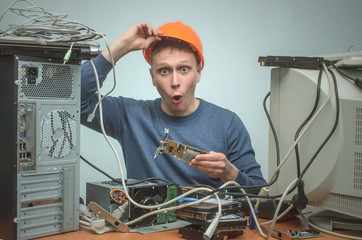 Surprised Computer technician in hard hat is installing a new video card into computer. PC repair service center.