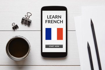 Learn French concept on smart phone screen with office objects on white wooden table. All screen content is designed by me. Flat lay