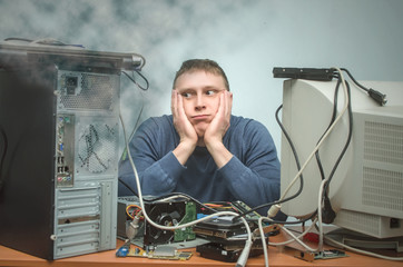 Tired and bored computer repairman is sitting on his workplace in smoke of burning hardware. Computer technician tired from his work and users. PC repair service center.