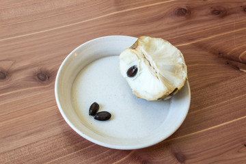 Simple piece of cherimoya fruit Annona cherimola and seeds on shallow dish, centered, wood background, horizontal aspect